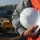 a Health & Safety Competent Person stands in front of the frame holding a hard hat