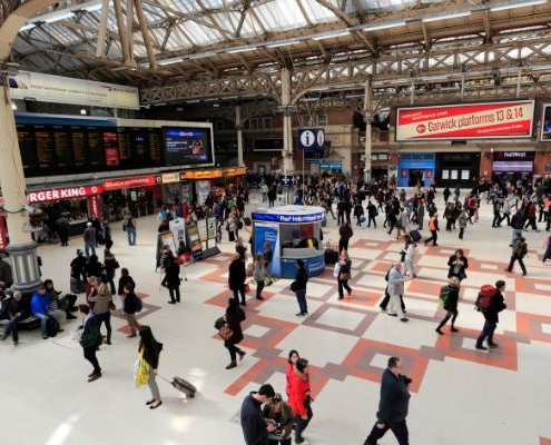 a busy concourse of a uk train station. The image shows people waiting for trains and the display board with the rail departures