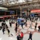 a busy concourse of a uk train station. The image shows people waiting for trains and the display board with the rail departures